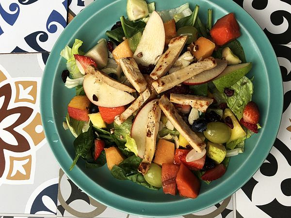 Ensalada de hojas verdes con fruta fresca y tiras de pollo a la plancha.