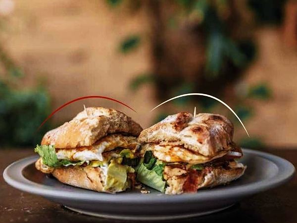 Lonche partido a la mitad con pollo, tocino, huevo estrellado y lechuga.