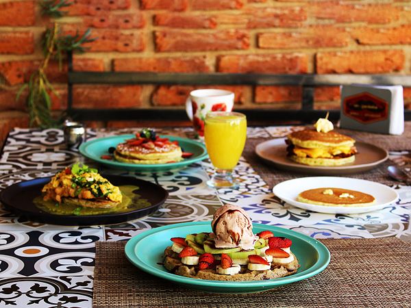 Mesa de Mr. Pankeke con waffle de frutas y helado, pankekes, chilaquiles, jugo de naranja y café, frente a una pared de ladrillo.