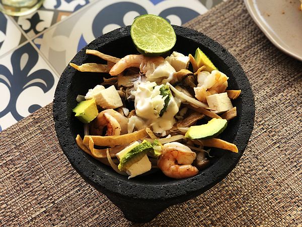 Sopa azteca en molcajete con tiras de tortilla, aguacate, queso panela, crema y camarones.